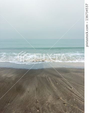Soft waves lap the shore on a quiet beach in early morning light with clouds in the sky reflecting on the water's surface Soft waves lap the shore on a quiet beach in early morning light with clouds in the sky reflecting on the water's surface 136734537