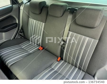 Back seat of a car with fabric seats featuring stripes and seat belts, showing simple seating layout and design in daylight Back seat of a car with fabric seats featuring stripes and seat belts, showing simple seating layout and design in daylight 136734540