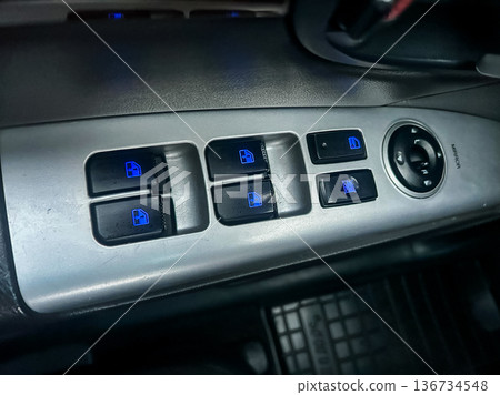 Control panel for car windows with buttons illuminated in blue, showing design and layout, taken during the day inside a vehicle 136734548
