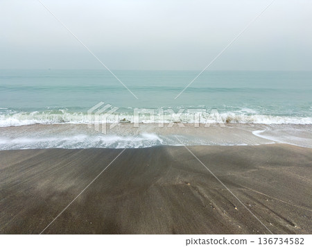 Waves roll onto the shore at a quiet beach during early morning hours with soft gray skies above Waves roll onto the shore at a quiet beach during early morning hours with soft gray skies above 136734582