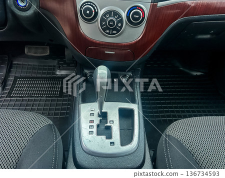 Close view of car interior showing gear shift, climate controls, and seat details at a parking area 136734593
