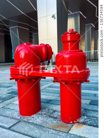 Bright red fire hydrant stands on pavement near a modern building in a city setting during daylight 136734594