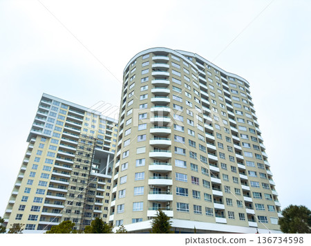 High-rise buildings stand in a city landscape under overcast skies in a suburban area, showcasing modern architecture and residential units High-rise buildings stand in a city landscape under overcast skies in a suburban area, showcasing modern architecture and residential units 136734598