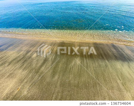 Calm water meets sandy shore on a sunny day at the beach with gentle waves in the afternoon light Calm water meets sandy shore on a sunny day at the beach with gentle waves in the afternoon light 136734604