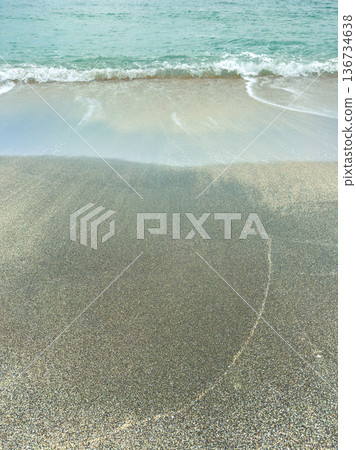 Waves wash onto a sandy beach with gentle surf at midday, creating patterns on the shore near the calm ocean water in a coastal area Waves wash onto a sandy beach with gentle surf at midday, creating patterns on the shore near the calm ocean water in a coastal area 136734638