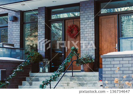 Decorative entrance in winter with dark bricks, wooden doors, wreath, and green garland near a snowy outdoor setting 136734647