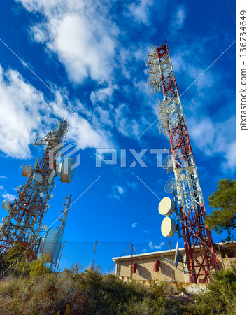 Two tall communication towers standing against a blue sky with clouds in a remote area during daylight Two tall communication towers standing against a blue sky with clouds in a remote area during daylight 136734649