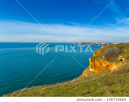 Coastal view shows cliffs and blue water under a clear sky in the afternoon near a wind farm in the distance Coastal view shows cliffs and blue water under a clear sky in the afternoon near a wind farm in the distance 136734669