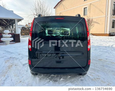 Black vehicle parked in snow-covered area near building during winter season with visible trees in the background 136734690