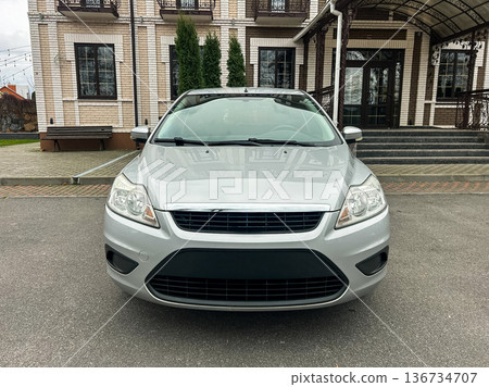 Silver car parked in front of a modern building with large windows and a covered entrance during a cloudy day 136734707