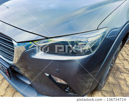 Close view of a gray car parked on a brick surface showing the front headlight and the hood during a clear day Close view of a gray car parked on a brick surface showing the front headlight and the hood during a clear day 136734714