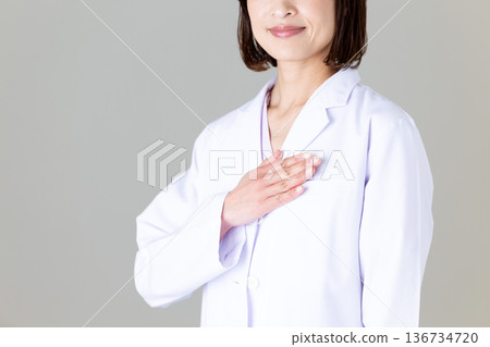 A middle-aged female doctor in a white coat holding her hand on her chest 136734720
