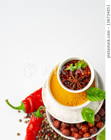 Spices and herbs arranged on bowls with red chili peppers and nuts on a white background 136734851