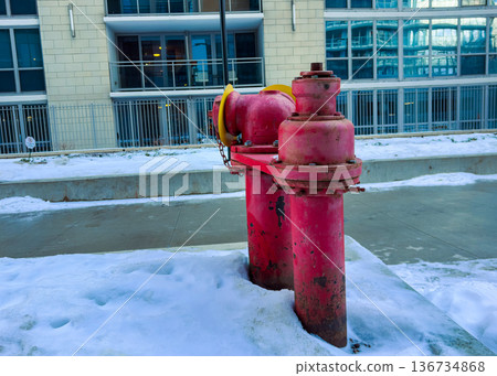 A bright red fire hydrant stands on the snow-covered ground near modern apartment buildings in a city during winter A bright red fire hydrant stands on the snow-covered ground near modern apartment buildings in a city during winter 136734868