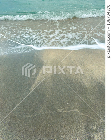 Waves rolling onto a sandy beach with light blue water during daylight hours Waves rolling onto a sandy beach with light blue water during daylight hours 136734870