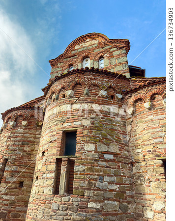 Old stone church stands in clear sky, showing brick patterns and architectural details in a small village during daytime Old stone church stands in clear sky, showing brick patterns and architectural details in a small village during daytime 136734903