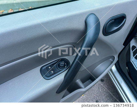Close view of a car door interior showing the window switch and door handle with part of the car visible in the background Close view of a car door interior showing the window switch and door handle with part of the car visible in the background 136734918