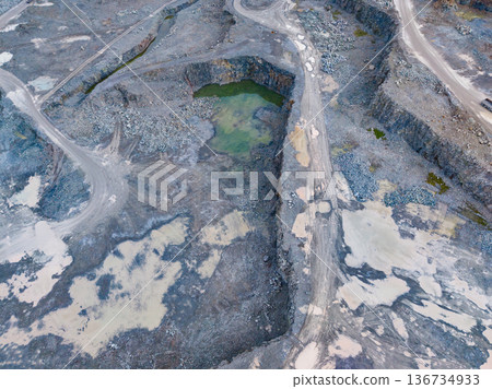 Quarry site with large open pit and water collection during daylight hours in a rocky area 136734933