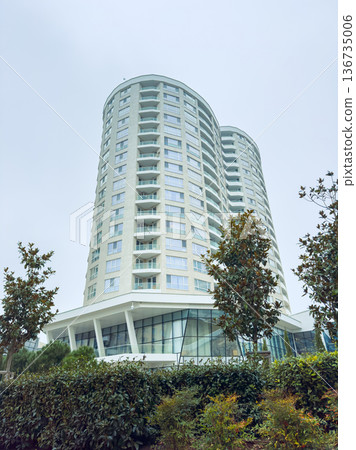 Modern building stands tall in urban area with trees and plants around on a cloudy day Modern building stands tall in urban area with trees and plants around on a cloudy day 136735006