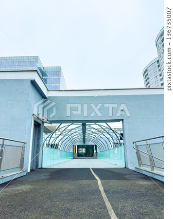 Path leading to a modern building structure with glass walls and metal framework in a city on a cloudy day Path leading to a modern building structure with glass walls and metal framework in a city on a cloudy day 136735007