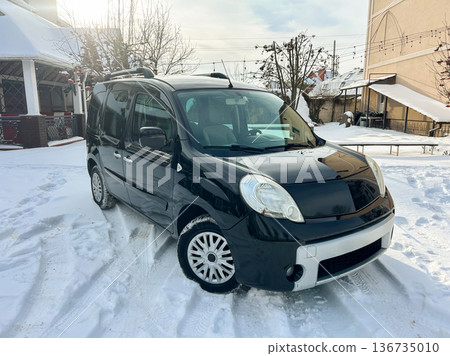 Black van parked in snowy area with trees and buildings nearby during daylight hours 136735010