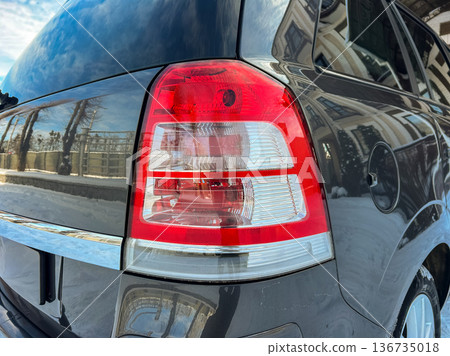 Close view of a car tail light showcasing design and details under clear skies with reflections visible on the vehicle surface 136735018