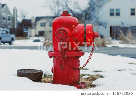 Bright red fire hydrant stands on snow-covered ground near houses and a street in a suburban area during winter Bright red fire hydrant stands on snow-covered ground near houses and a street in a suburban area during winter 136735020