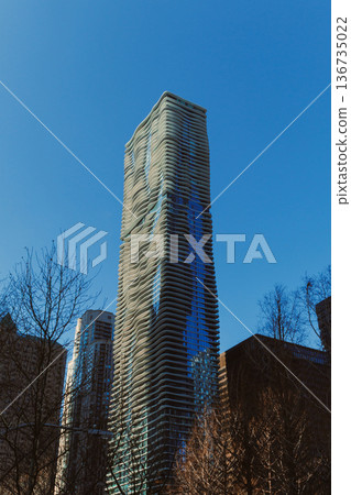Tall modern building in an urban area under a clear blue sky with sunlight shining on the glass 136735022