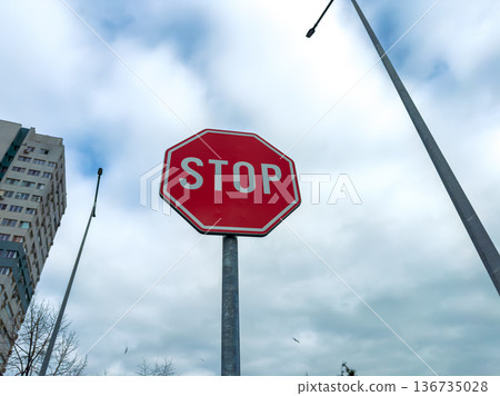 Stop sign stands tall beside tall buildings and street lamps under a cloudy sky in an urban area during the day Stop sign stands tall beside tall buildings and street lamps under a cloudy sky in an urban area during the day 136735028