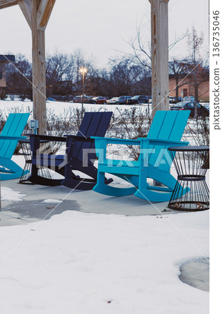 Colorful chairs on a patio with snow covering the ground in a quiet outdoor space during winter at dusk near a small town Colorful chairs on a patio with snow covering the ground in a quiet outdoor space during winter at dusk near a small town 136735046