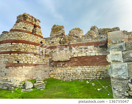 Ruins of an ancient stone structure with grass and blue sky visible in the background during daytime hours 136735047