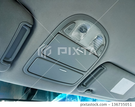 Interior view of a car's overhead control panel with lights and switches located above the driver's seat for adjusting settings and lighting Interior view of a car's overhead control panel with lights and switches located above the driver's seat for adjusting settings and lighting 136735051