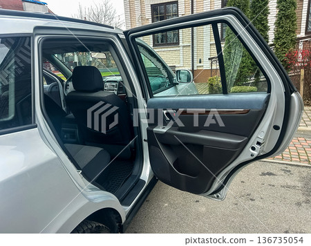 Car door is open beside a building and a parking area on a cloudy day showing the inside of the vehicle 136735054