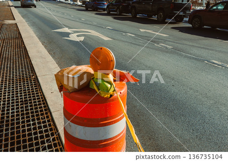 Traffic safety equipment is placed on a construction cone on a busy street with vehicles and lanes marked near a construction area during daylight Traffic safety equipment is placed on a construction cone on a busy street with vehicles and lanes marked near a construction area during daylight 136735104