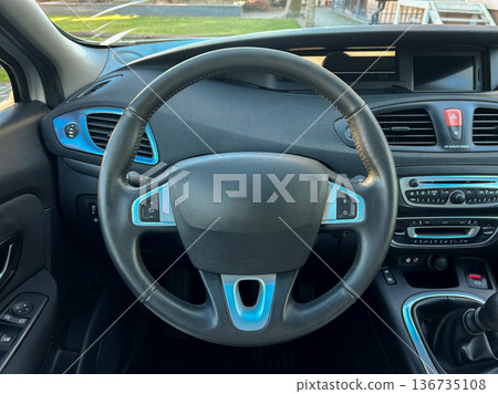 Car interior view with steering wheel and dashboard at a parking lot during afternoon Car interior view with steering wheel and dashboard at a parking lot during afternoon 136735108
