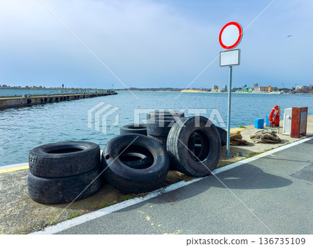 Old tires are stacked near the harbor by the water under a cloudy sky with a no entry sign beside them Old tires are stacked near the harbor by the water under a cloudy sky with a no entry sign beside them 136735109