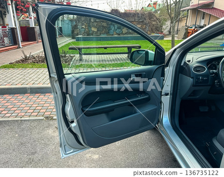 Car door is open outside a building with a lawn and benches during the day showing the interior of the vehicle and the surrounding area Car door is open outside a building with a lawn and benches during the day showing the interior of the vehicle and the surrounding area 136735122