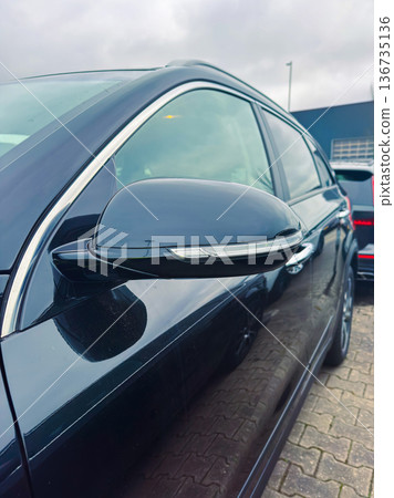 Black car parked in a lot with focus on side mirror and clouds in the sky Black car parked in a lot with focus on side mirror and clouds in the sky 136735136