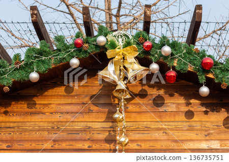 Festive christmas garland with gold bells on wooden cabin roof at outdoors Christmas market Festive christmas garland with gold bells on wooden cabin roof at outdoors Christmas market 136735751