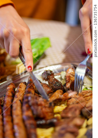 Hands cutting grilled sausage and meat platter at restaurant Hands cutting grilled sausage and meat platter at restaurant 136735754