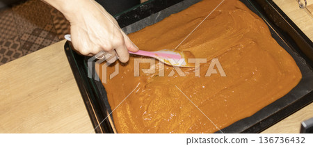 Person spreads, brown, heavy, sugary cream on a baking tray Person spreads, brown, heavy, sugary cream on a baking tray 136736432