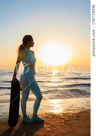 Fit young woman is posing against sea background. Sporty female with skateboard on the seaside promenade. Fit young woman is posing against sea background. Sporty female with skateboard on the seaside promenade. 136738096