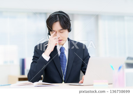 A young Japanese man wearing a headset and thinking about his computer in the office 136738699