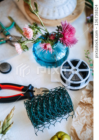 High angle view of florist tools and materials including wire mesh and flowers on table. Eco-friendly floristry, sustainable floral design, chicken wire technique, plastic-free mechanics. High angle view of florist tools and materials including wire mesh and flowers on table. Eco-friendly floristry, sustainable floral design, chicken wire technique, plastic-free mechanics. 136738824
