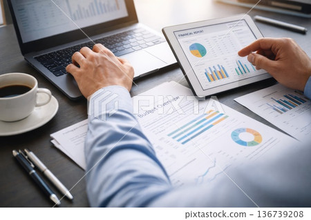 Business professional analyzing financial data on tablet and laptop with reports on desk 136739208