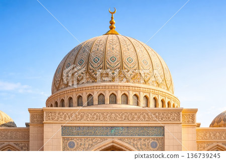 Ornate mosque dome with intricate patterns and golden crescent against blue sky 136739245