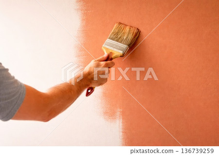 Hand painting wall with brush applying warm orange paint on white surface Hand painting wall with brush applying warm orange paint on white surface 136739259