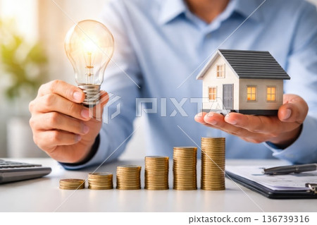 Energy efficient home concept with light bulb and house model over stacked coins 136739316