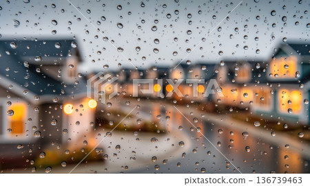 Rain droplets on window glass with blurred houses and lights background Rain droplets on window glass with blurred houses and lights background 136739463
