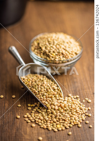 Uncooked green lentil on scoop on wooden table. Uncooked green lentil on scoop on wooden table. 136742024